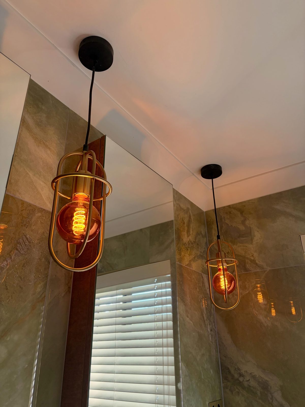 Gold cage pendant lights with warm Edison bulbs above a marble-tiled ensuite