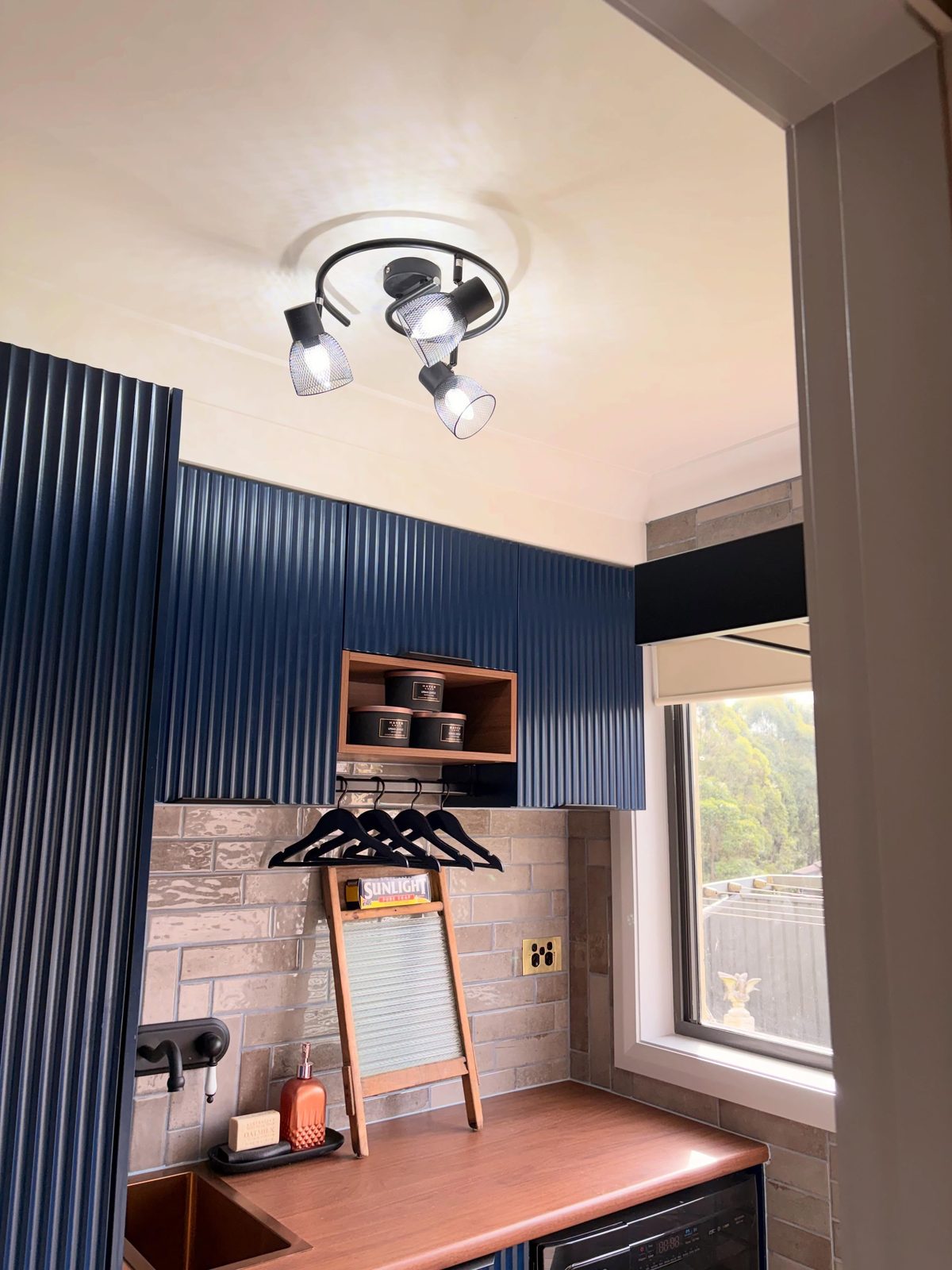 Three-light adjustable track spotlight fitted to the ceiling of a modern navy laundry